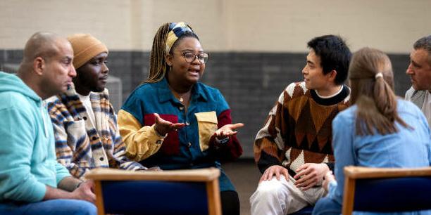 Medium shot of a group of adults sitting in a circle and talking to each other about their mental well-being. They are all wearing casual clothing. The community centre is located in Seaton Deleval in the North East of England.